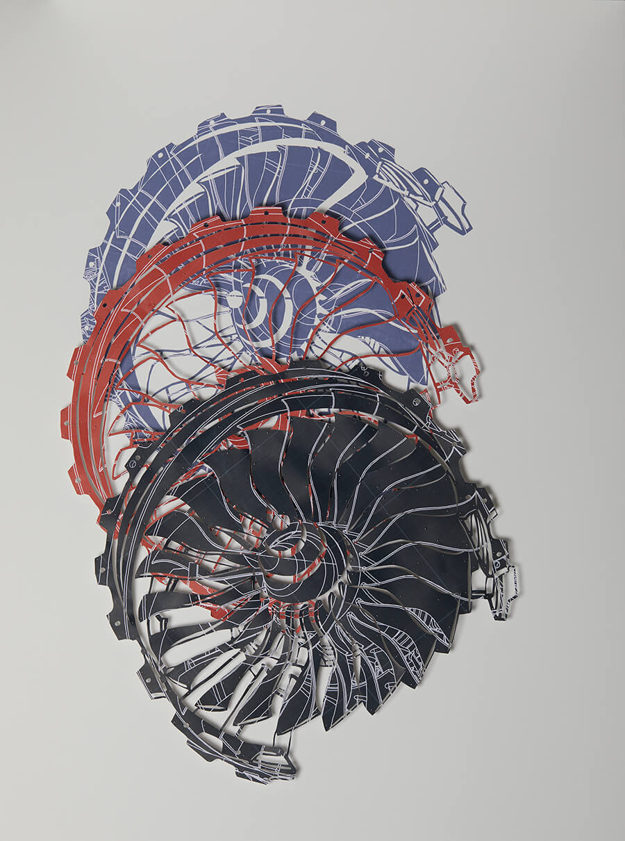 Burning From Within I by Claire Brewster. An intricate paper sculpture depicting the front intake view of a gas turbine engine. Three layers of hand-cut archival prints in blue, red, and black are stacked to create a swirling, radial composition of turbine blades. The 122cm x 91.5cm artwork is pinned to the wall, creating a three-dimensional effect with cast shadows.