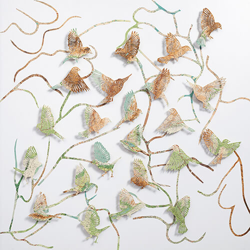 Seeing The Future by Claire Brewster. A large paper sculpture of birds flying among winding, branch-like paths, hand-cut from pages of a vintage The Times Atlas in earthy green and brown tones.