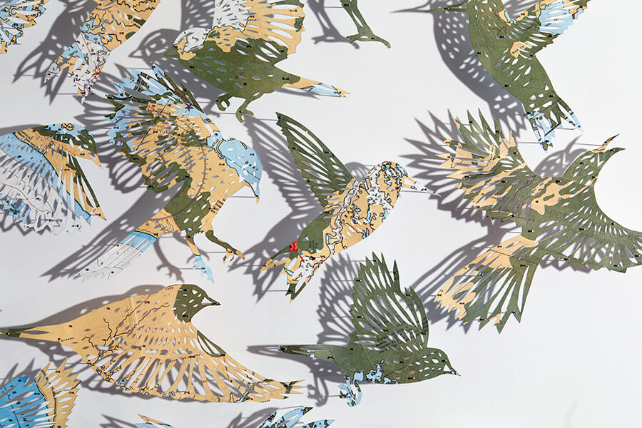 A detail of "A Confluence by Claire Brewster. A paper sculpture featuring a swirling flock of birds hand-cut from a vintage map of Florida in blue, tan, and green tones, commissioned for the Orlando Championsgate hotel."