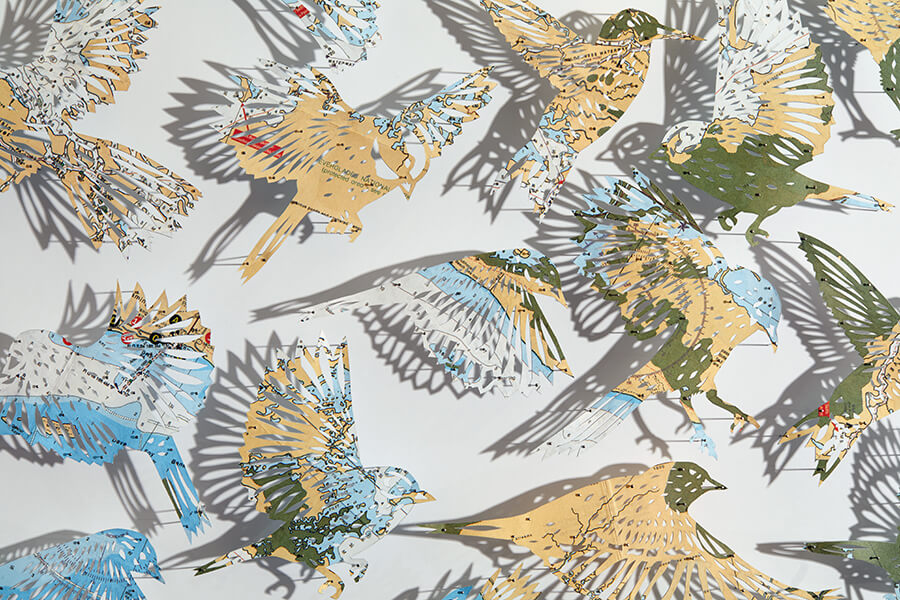 A detail of "A Confluence by Claire Brewster. A paper sculpture featuring a swirling flock of birds hand-cut from a vintage map of Florida in blue, tan, and green tones, commissioned for the Orlando Championsgate hotel."