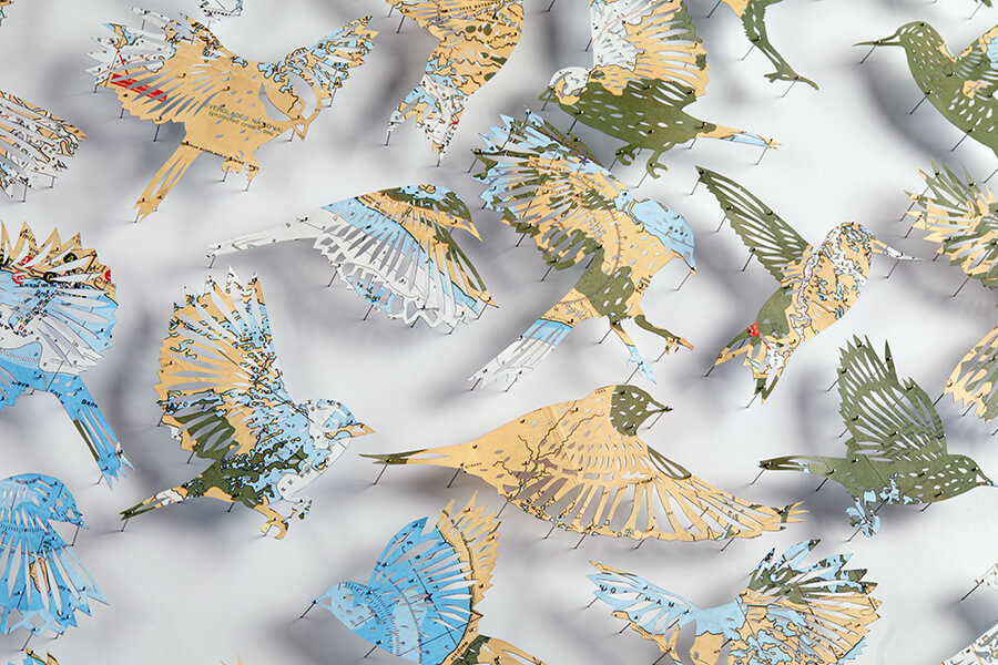 A detail of "A Confluence by Claire Brewster. A paper sculpture featuring a swirling flock of birds hand-cut from a vintage map of Florida in blue, tan, and green tones, commissioned for the Orlando Championsgate hotel."
