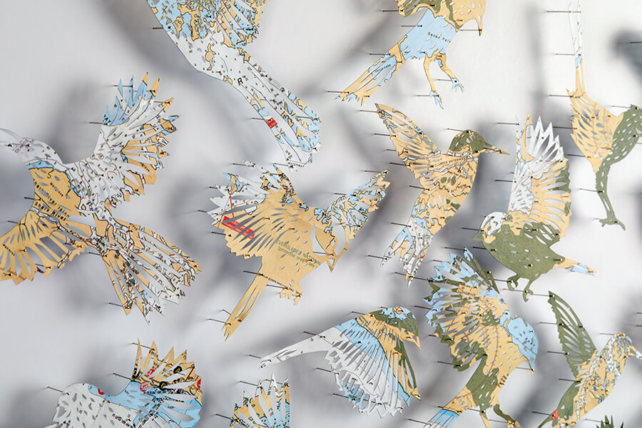 A detail of "A Confluence by Claire Brewster. A paper sculpture featuring a swirling flock of birds hand-cut from a vintage map of Florida in blue, tan, and green tones, commissioned for the Orlando Championsgate hotel."